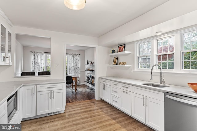 kitchen with a sink, light wood-type flooring, light countertops, white cabinets, and appliances with stainless steel finishes