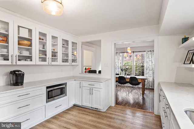 kitchen featuring stainless steel microwave, light wood-type flooring, white cabinetry, and glass insert cabinets
