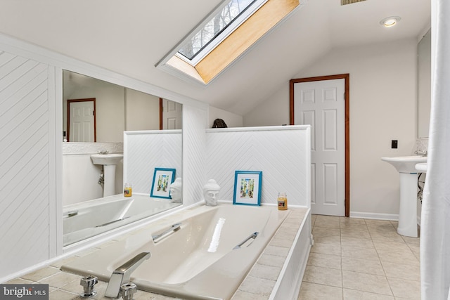 full bathroom featuring a garden tub, tile patterned floors, lofted ceiling with skylight, and baseboards