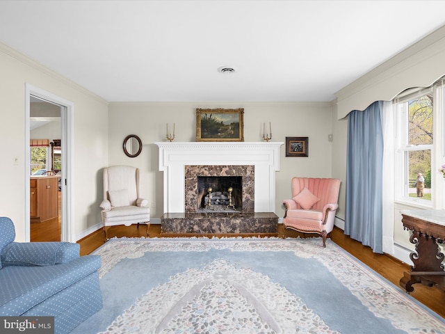 living room featuring visible vents, a fireplace, wood finished floors, baseboards, and ornamental molding