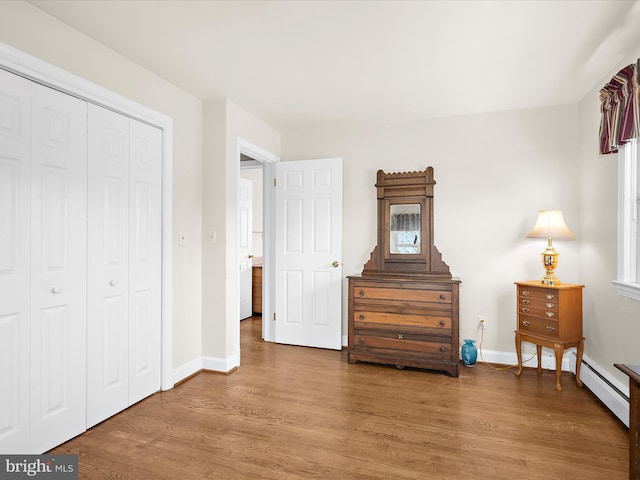 bedroom with baseboards, a baseboard radiator, a closet, and wood finished floors