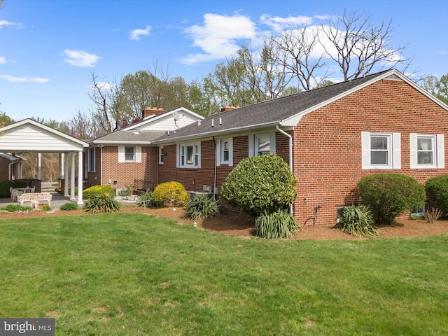rear view of house with a lawn, a carport, and brick siding