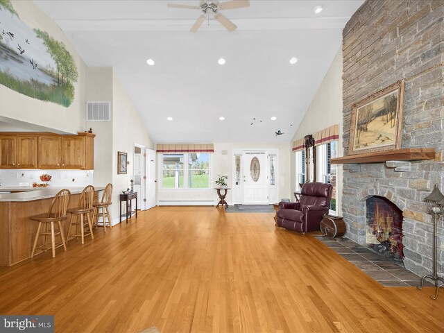 living area with high vaulted ceiling, a fireplace, light wood finished floors, and visible vents