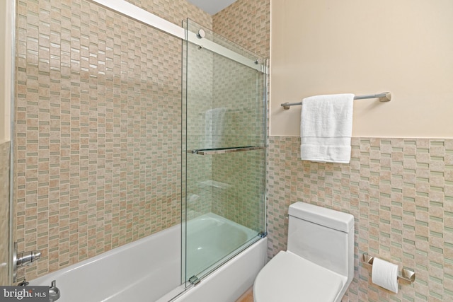 full bathroom featuring bath / shower combo with glass door, wainscoting, toilet, and tile walls