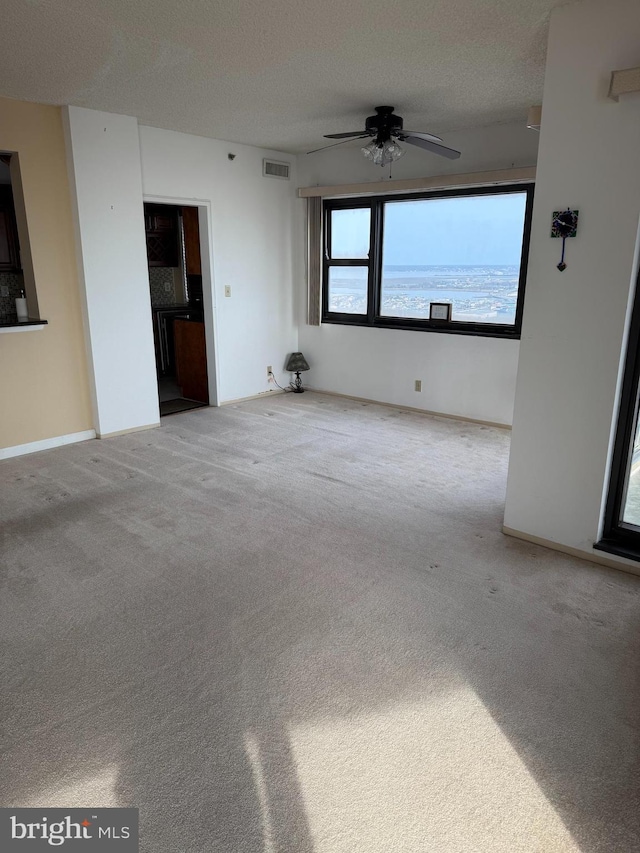 carpeted spare room with a ceiling fan, visible vents, and a textured ceiling