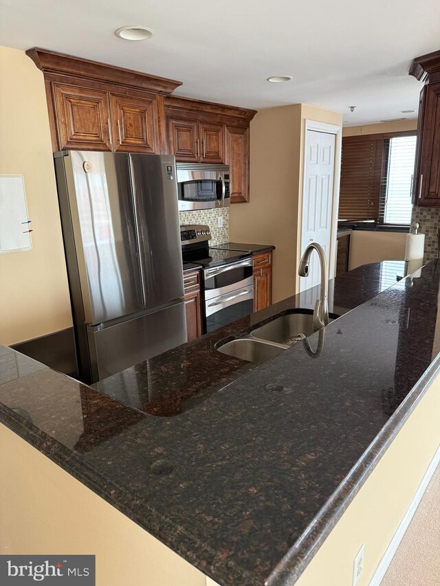 kitchen featuring decorative backsplash, dark stone counters, stainless steel appliances, and a sink