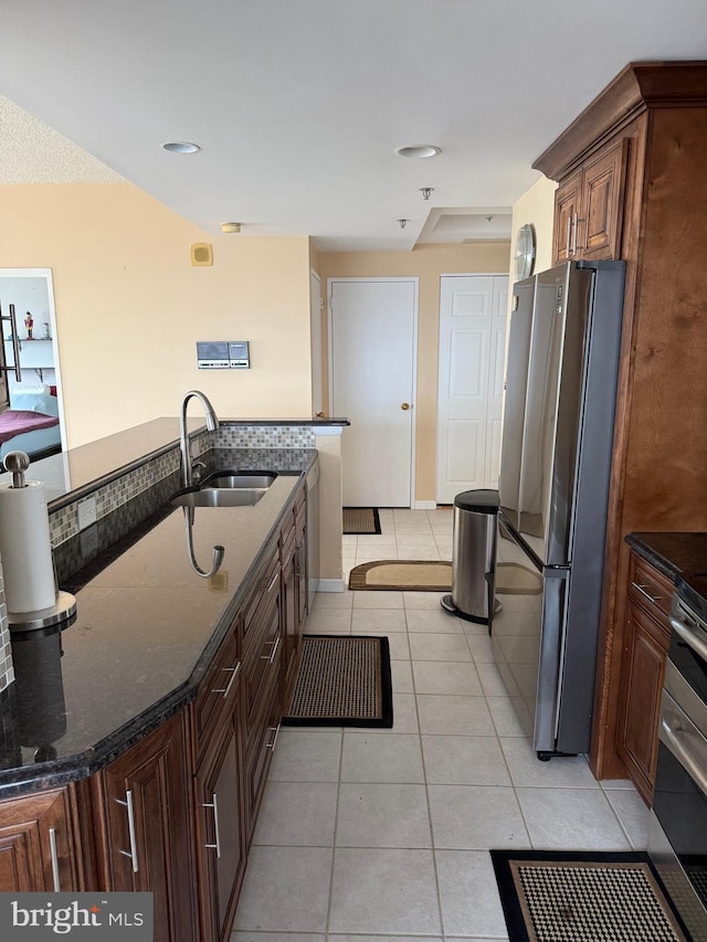 kitchen with light tile patterned floors, dark stone countertops, a sink, and freestanding refrigerator
