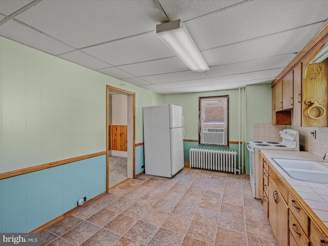 kitchen with white appliances, a drop ceiling, radiator heating unit, tile counters, and a sink