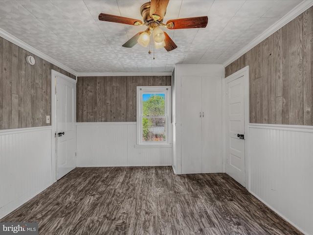 empty room featuring a ceiling fan, wood walls, wood finished floors, and a wainscoted wall