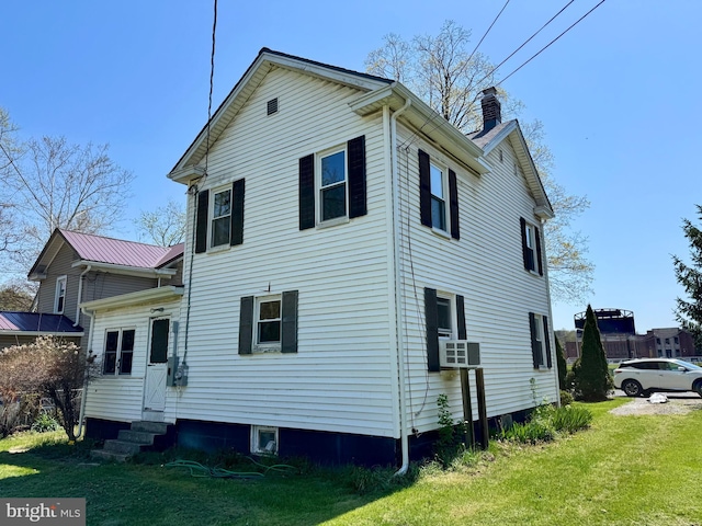 back of house featuring entry steps, a chimney, and a yard