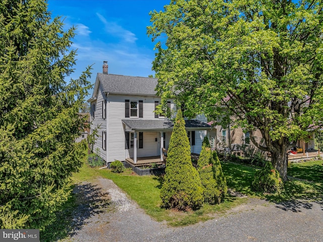 view of front of home with covered porch, a front yard, a chimney, and roof with shingles