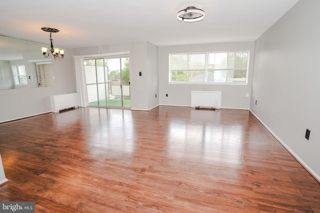 unfurnished living room featuring a chandelier, wood finished floors, radiator, and baseboards