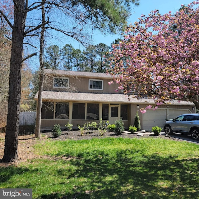 traditional home with a sunroom, a garage, roof with shingles, and a front yard