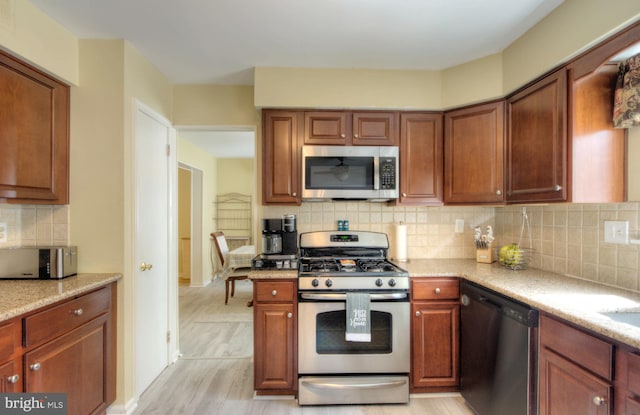 kitchen with appliances with stainless steel finishes, decorative backsplash, light wood-style flooring, and light stone counters