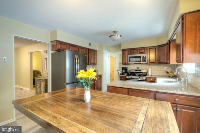 kitchen with decorative backsplash, appliances with stainless steel finishes, a sink, baseboards, and light wood-style flooring