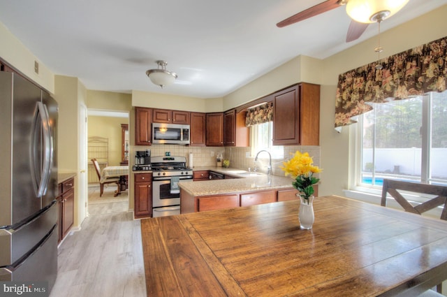 kitchen featuring a ceiling fan, backsplash, appliances with stainless steel finishes, light wood-type flooring, and a sink