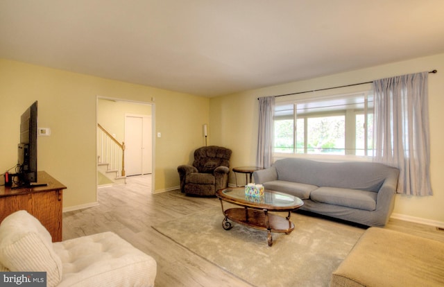 living area with baseboards, stairway, and light wood-type flooring