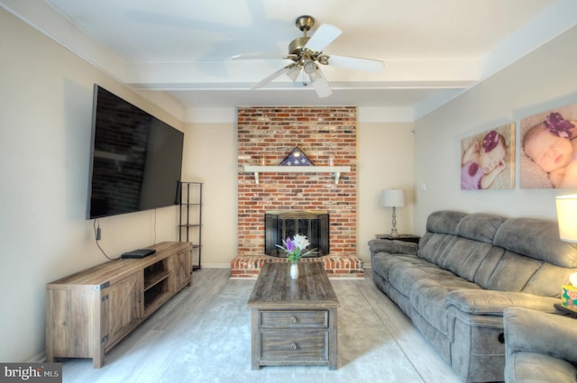 living room featuring ceiling fan, a brick fireplace, light wood-type flooring, beam ceiling, and baseboards