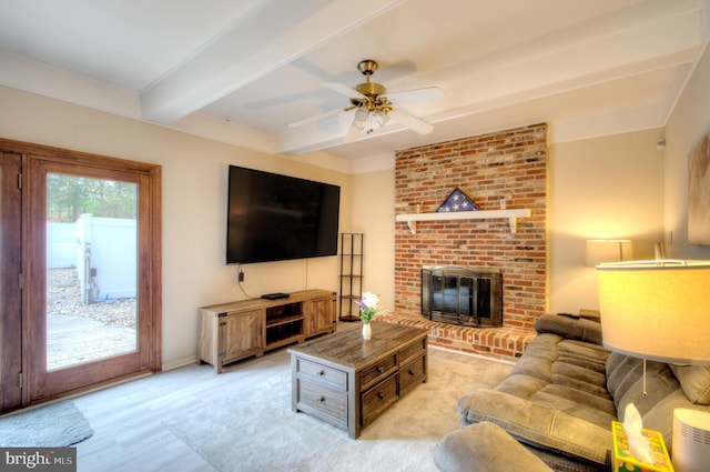 living room with a ceiling fan, a fireplace, baseboards, beamed ceiling, and light wood-style flooring