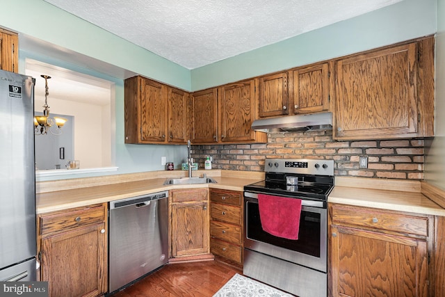 kitchen featuring appliances with stainless steel finishes, under cabinet range hood, a sink, light countertops, and a textured ceiling