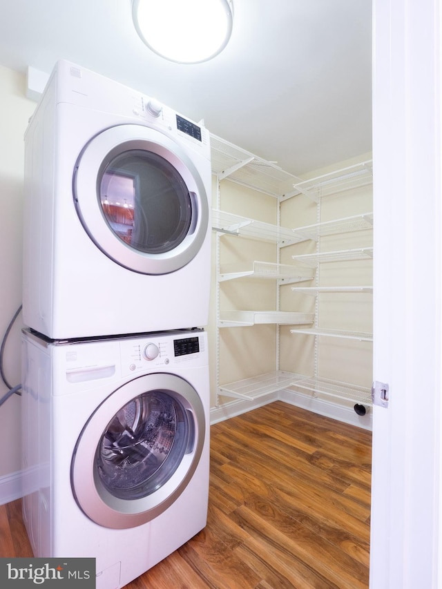 clothes washing area featuring stacked washing maching and dryer, laundry area, and wood finished floors