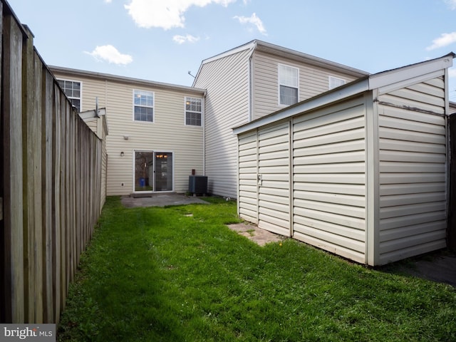 back of property with central AC unit, fence, and a lawn