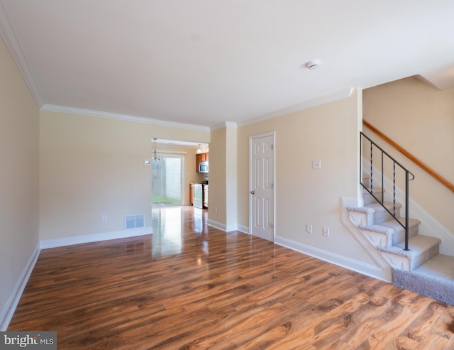 unfurnished living room with baseboards, crown molding, stairs, visible vents, and wood finished floors