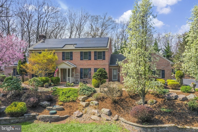 colonial inspired home with brick siding, roof mounted solar panels, and a chimney