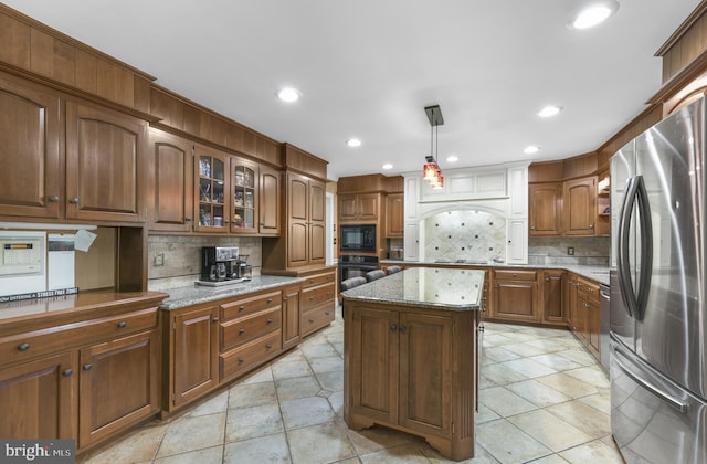 kitchen featuring brown cabinetry, black appliances, decorative backsplash, glass insert cabinets, and light stone countertops