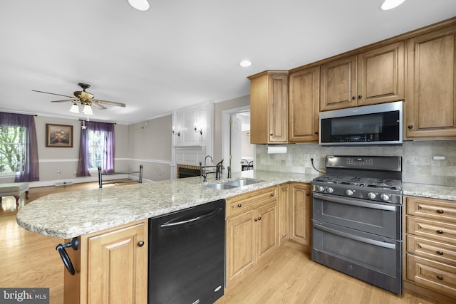 kitchen with stainless steel appliances, a peninsula, light wood-style flooring, a sink, and a ceiling fan