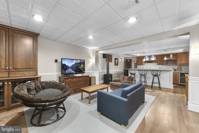living room with recessed lighting, wine cooler, a wood stove, visible vents, and light wood-type flooring