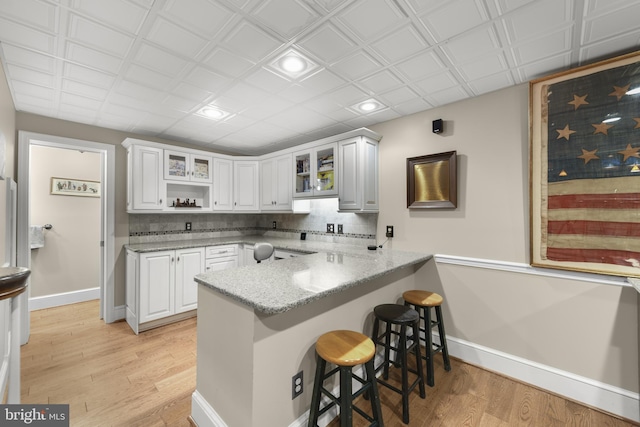 kitchen with a peninsula, baseboards, a kitchen breakfast bar, and light wood finished floors