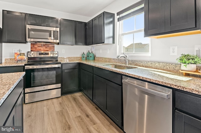 kitchen with stainless steel appliances, light wood finished floors, a sink, and light stone counters
