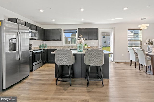 kitchen with light stone countertops, recessed lighting, a kitchen island, appliances with stainless steel finishes, and a breakfast bar area