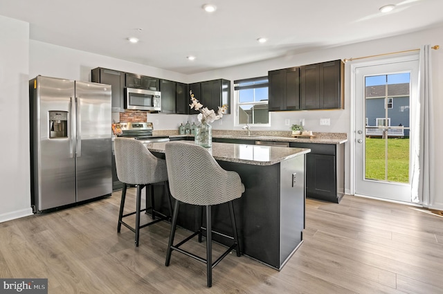 kitchen with a center island, light wood-type flooring, a breakfast bar, light stone countertops, and stainless steel appliances