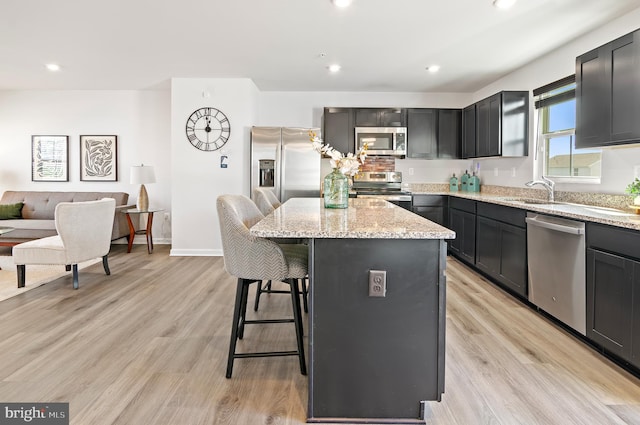 kitchen featuring light stone countertops, light wood-style flooring, a kitchen island, stainless steel appliances, and a breakfast bar area