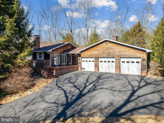 view of front of house featuring a garage, brick siding, driveway, and a chimney