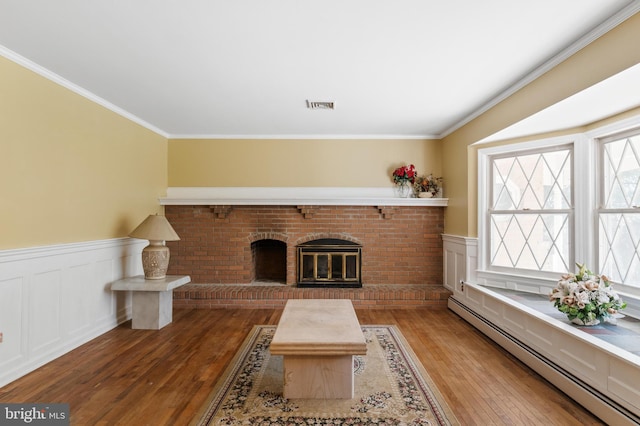 living area with visible vents, a brick fireplace, hardwood / wood-style flooring, a wainscoted wall, and a baseboard heating unit
