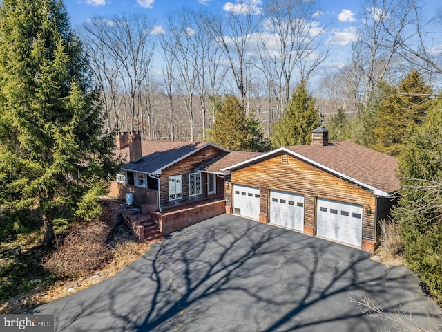 view of front facade with an attached garage, a shingled roof, a chimney, and driveway