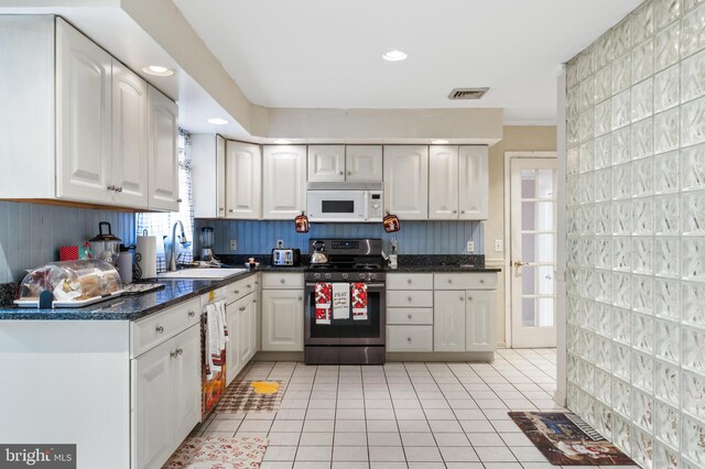 kitchen featuring gas stove, white microwave, light tile patterned floors, visible vents, and a sink