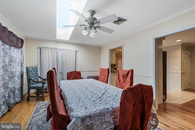 dining room with ceiling fan, visible vents, a wainscoted wall, a skylight, and hardwood / wood-style floors