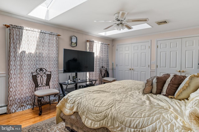 bedroom featuring visible vents, two closets, crown molding, wood finished floors, and a skylight