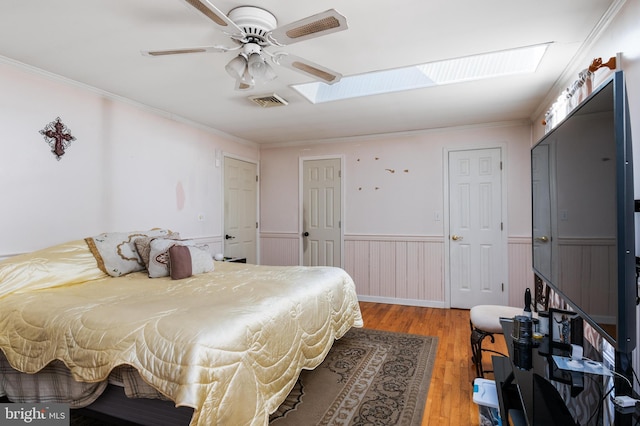 bedroom featuring light wood finished floors, ornamental molding, a wainscoted wall, and a skylight
