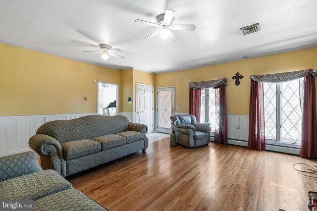 living room featuring a wealth of natural light, a ceiling fan, a wainscoted wall, and wood finished floors