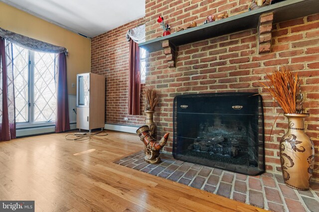 living area featuring a baseboard radiator, wood finished floors, brick wall, and a brick fireplace