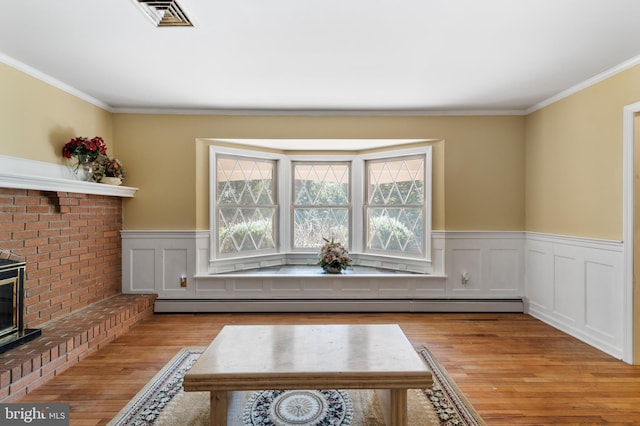 sitting room with light wood-style floors, visible vents, a baseboard radiator, and ornamental molding