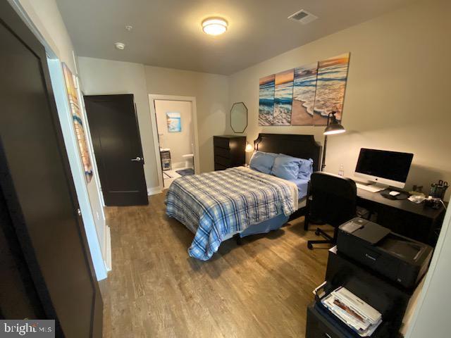 bedroom featuring wood finished floors, an office area, and ensuite bath