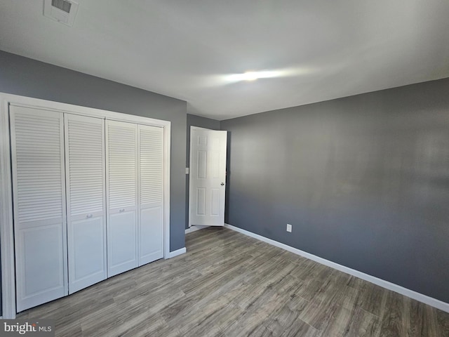 unfurnished bedroom featuring wood finished floors, baseboards, a closet, and visible vents