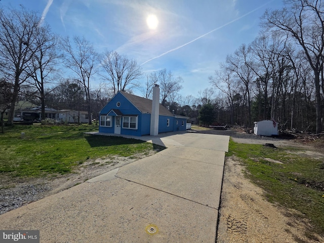 view of side of property featuring a yard, driveway, a chimney, and an outbuilding