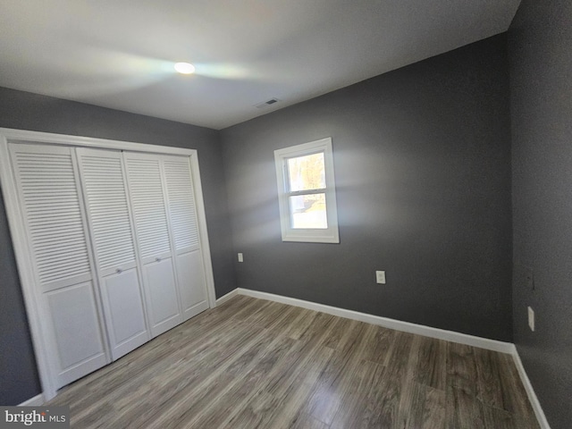 unfurnished bedroom with wood finished floors, baseboards, a closet, and visible vents